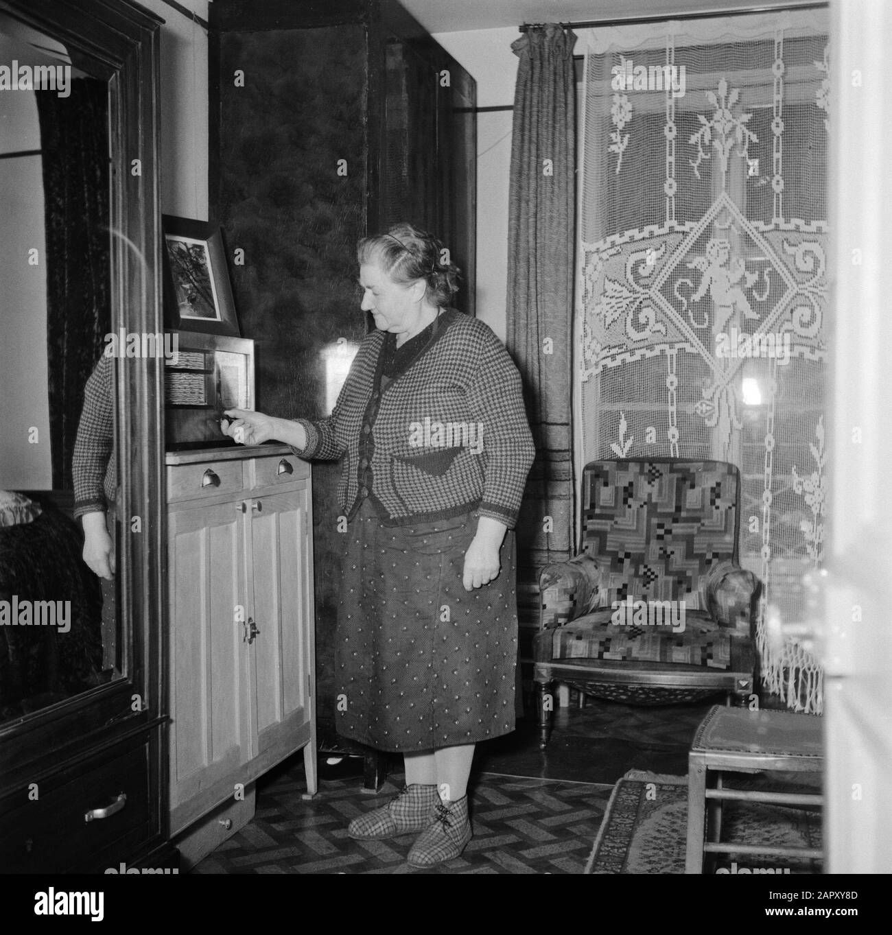 Residenti di un condominio a Parigi Donna gestisce la radio nel suo soggiorno Data: 1950 luogo: Francia, Parigi Parole Chiave: Interni, pantofole, radio set, donne Foto Stock