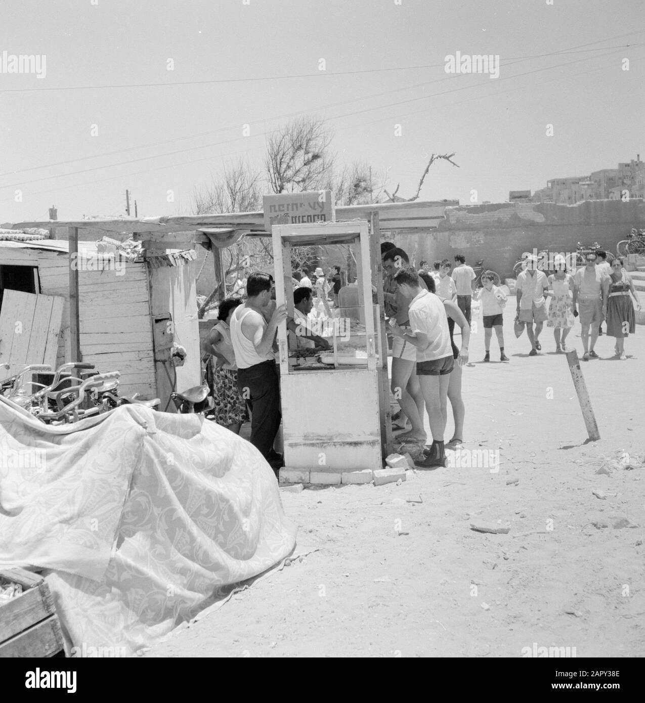 Israele 1964-1965: Tel Aviv, durante il Sabbath al mare la gente vestito Summerly compra il cibo sul bordo della spiaggia in una stalla costituita da porte e partizioni di legno Annotation: Durante il Sabbath attira molte persone da Tel Aviv al mare Date: 1964 Location: Israel, Tel Aviv Keywords: bagnanti, vita quotidiana, biciclette, paratie, spiagge, alimenti Foto Stock