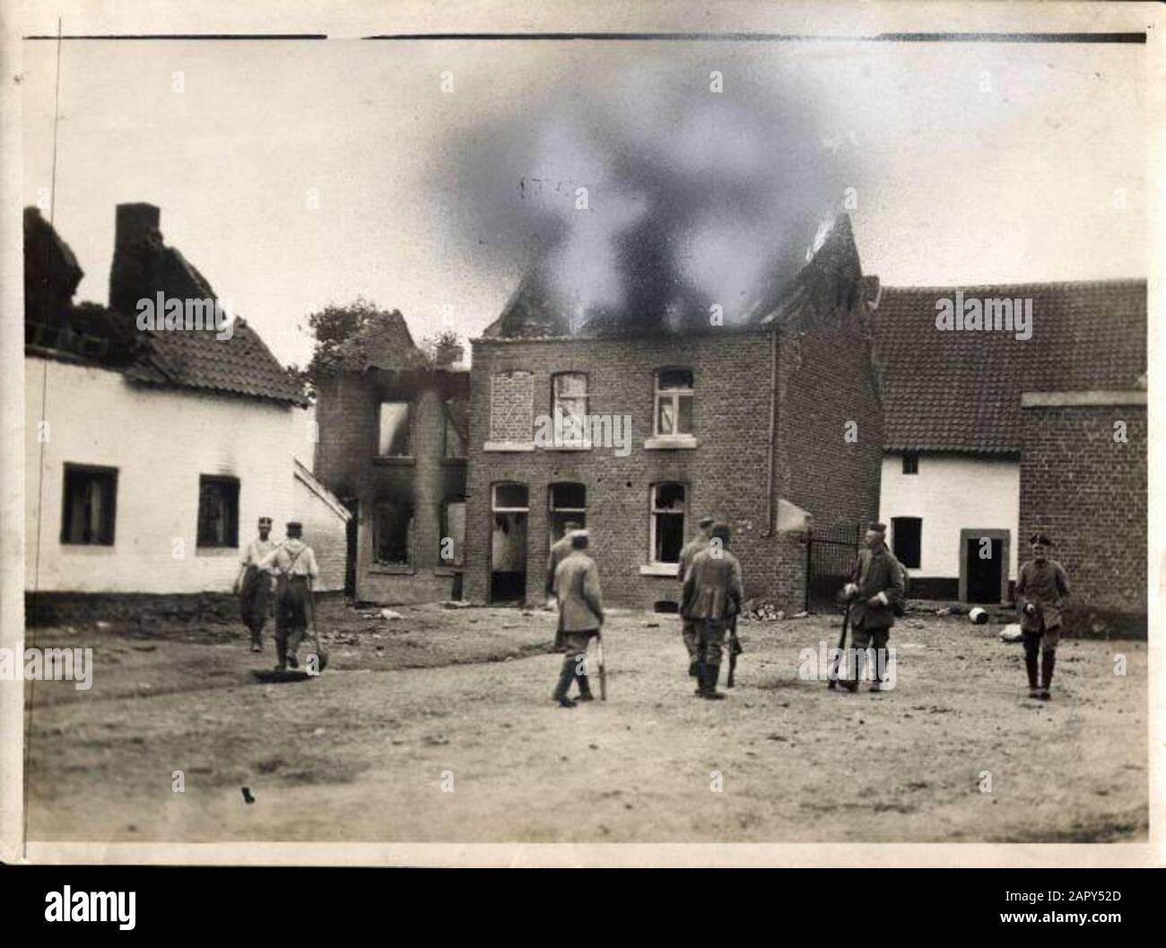 Prima guerra mondiale, guerra di terra; i tedeschi si muovono in Belgio appena oltre il confine vicino al Limburgo olandese, 1914. Una pattuglia tedesca con revolver disegnato ha appena lasciato la casa bruciante nel villaggio di Mouland. Che la casa bruciata luminosamente non era visibile sulla foto-stampa, secondo una nota sul retro, quindi fumo è stato applicato con vernice ritocco. Mouland, Belgio 1914. Foto Stock
