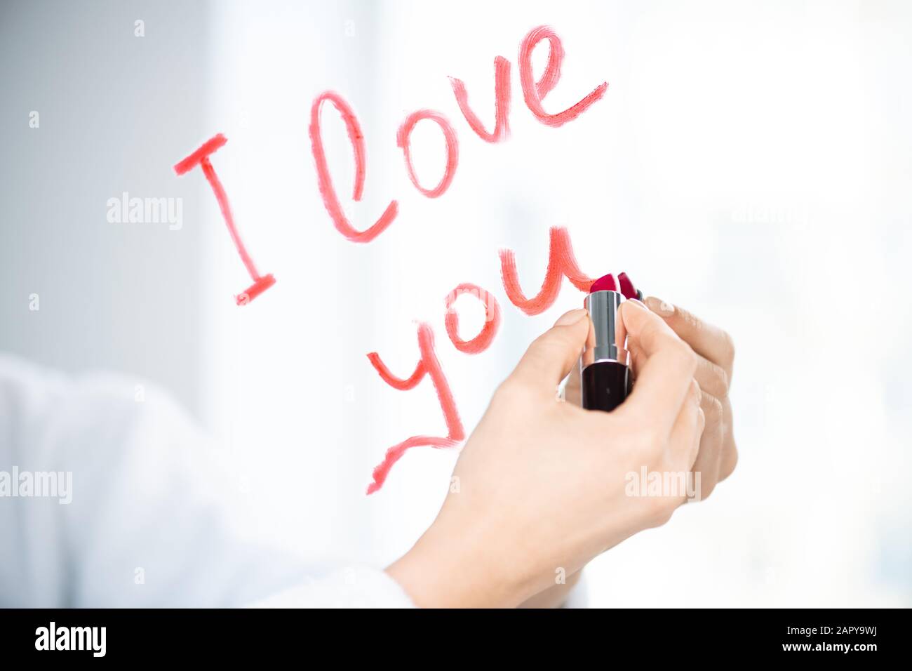 Mano di giovane donna che scrive il messaggio di amore con rossetto rosso o cremisi Foto Stock