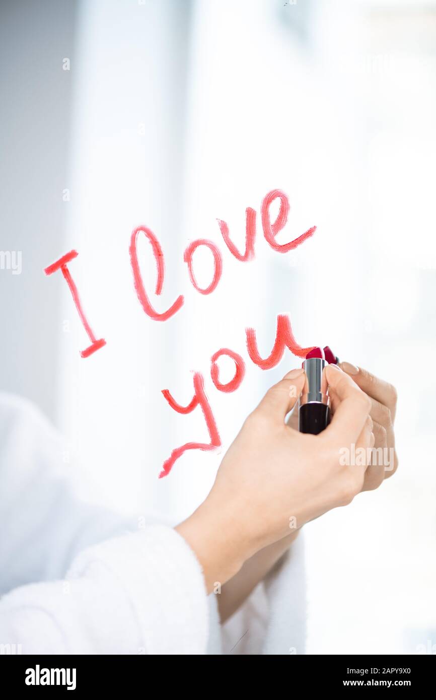 Mano di giovane amoroso femminile scrittura amore messaggio sullo specchio con rossetto Foto Stock