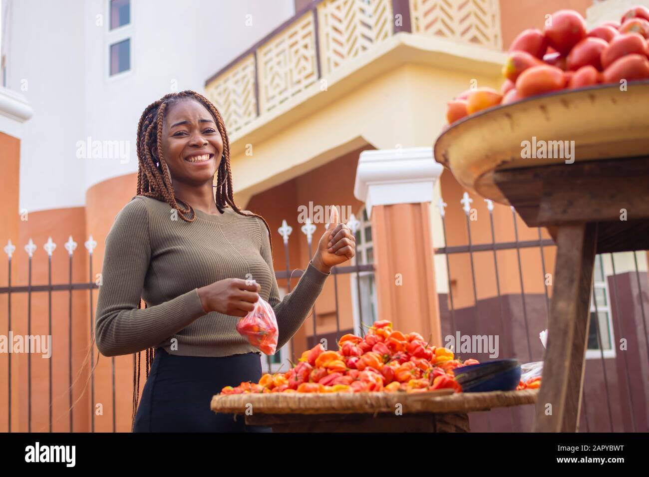 giovane donna nera che tiene i pomodori e dà i pollici in su nel mercato Foto Stock