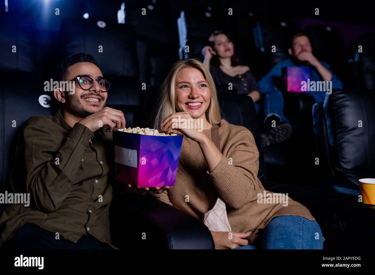 Allegra giovane coppia interculturale che si gode il tempo nel cinema mentre si mangia popcorn Foto Stock