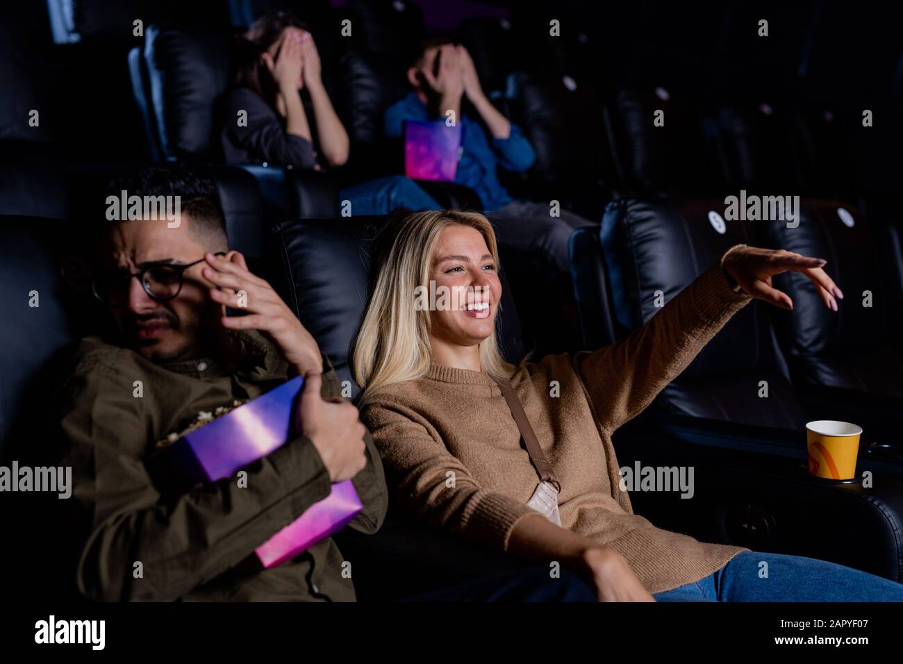 Giovane donna sorridente che punta a un grande schermo mentre guarda un film d'azione Foto Stock