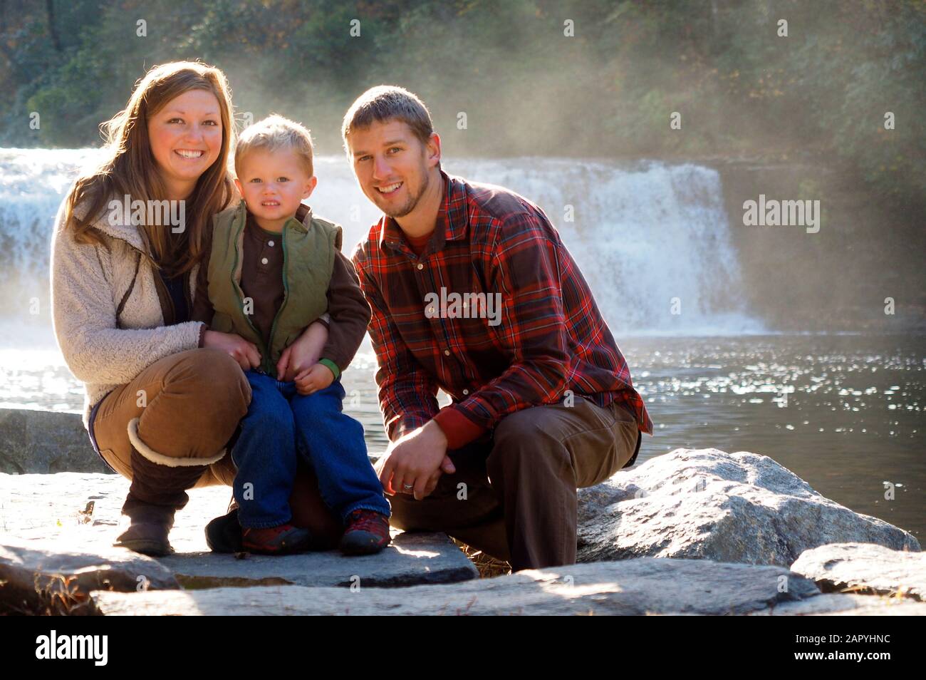 Ritratto di una famiglia in piedi sulle rocce con un cascata sullo sfondo sfocato Foto Stock