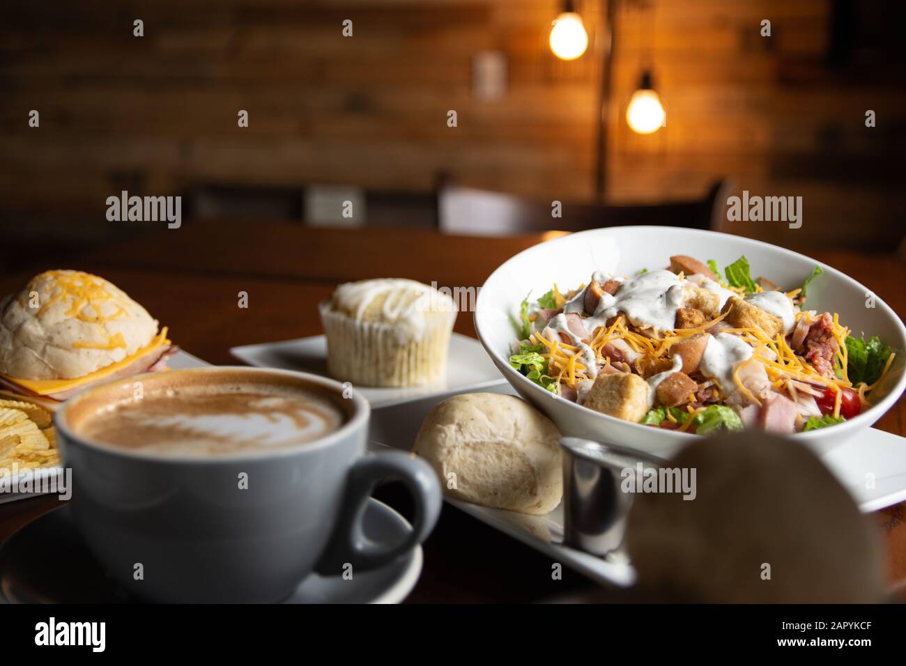 Caffè e cibo con luci arancioni sullo sfondo. Caffè, Cioccolata Calda, Insalata, Sandwich, Panini, Torte E Zuppa. Su un tavolo della caffetteria. Foto Stock