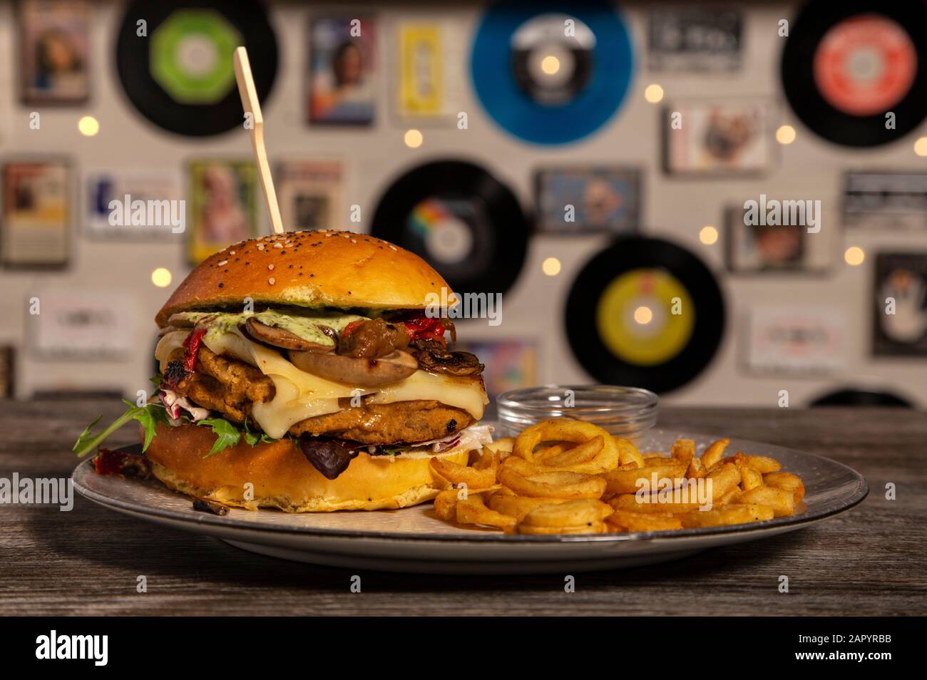 Hamburger vegan fatto in casa con ceci, funghi saltati, formaggio Emmenthal e patatine fritte su tavola di legno. Immagine isolata. Foto Stock