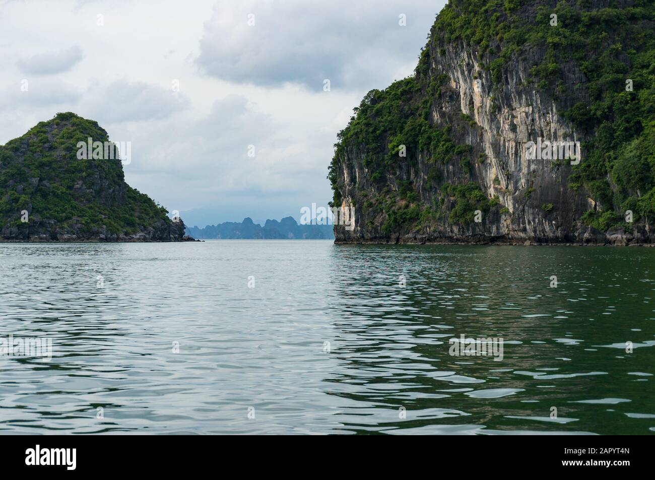 Stretto passaggio tra due isole di montagna con Halong Bay paesaggio in lontananza. Halong Bay, Vietnam Foto Stock