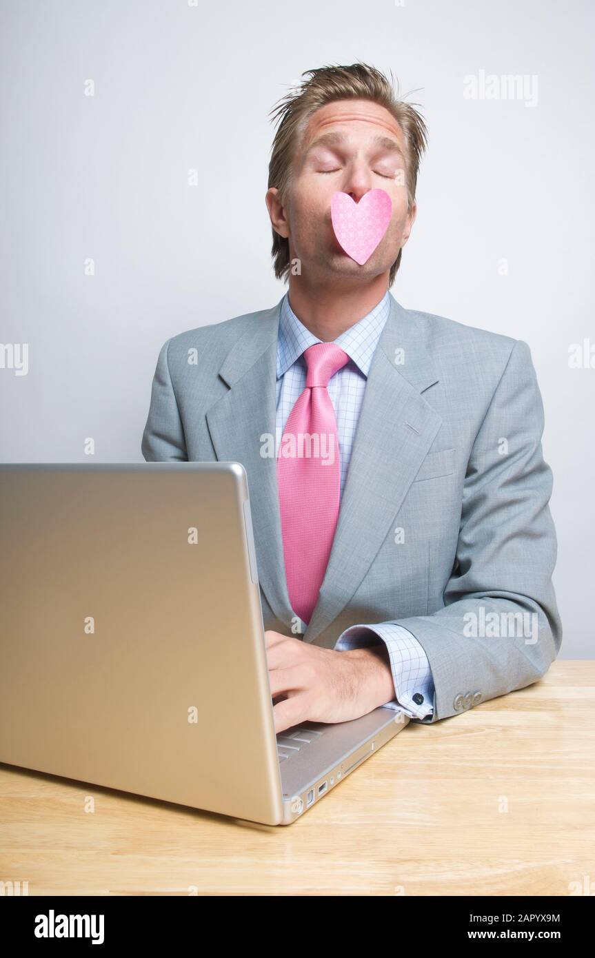 Flirty lavoratore di ufficio seduto alla sua scrivania con un cuore bloccato alle sue labbra Foto Stock