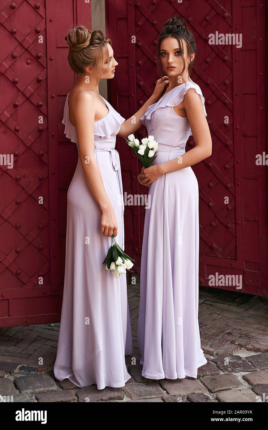 Due belle ragazze bridesmaids bionda e donne brunette indossare elegante lunghezza piena lavanda viola tulle una spalla abito da sposa e tenuta Foto Stock