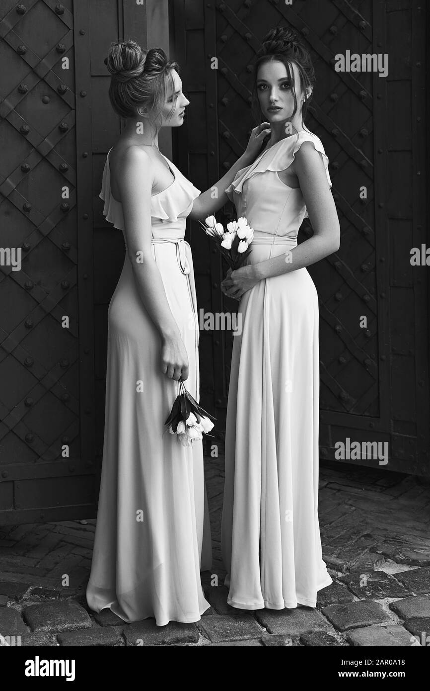 Due belle sposini ragazze bionde e donne brunette indossando elegante full length colore chiaro tulle una spalla abito da sposa e tenuta Foto Stock