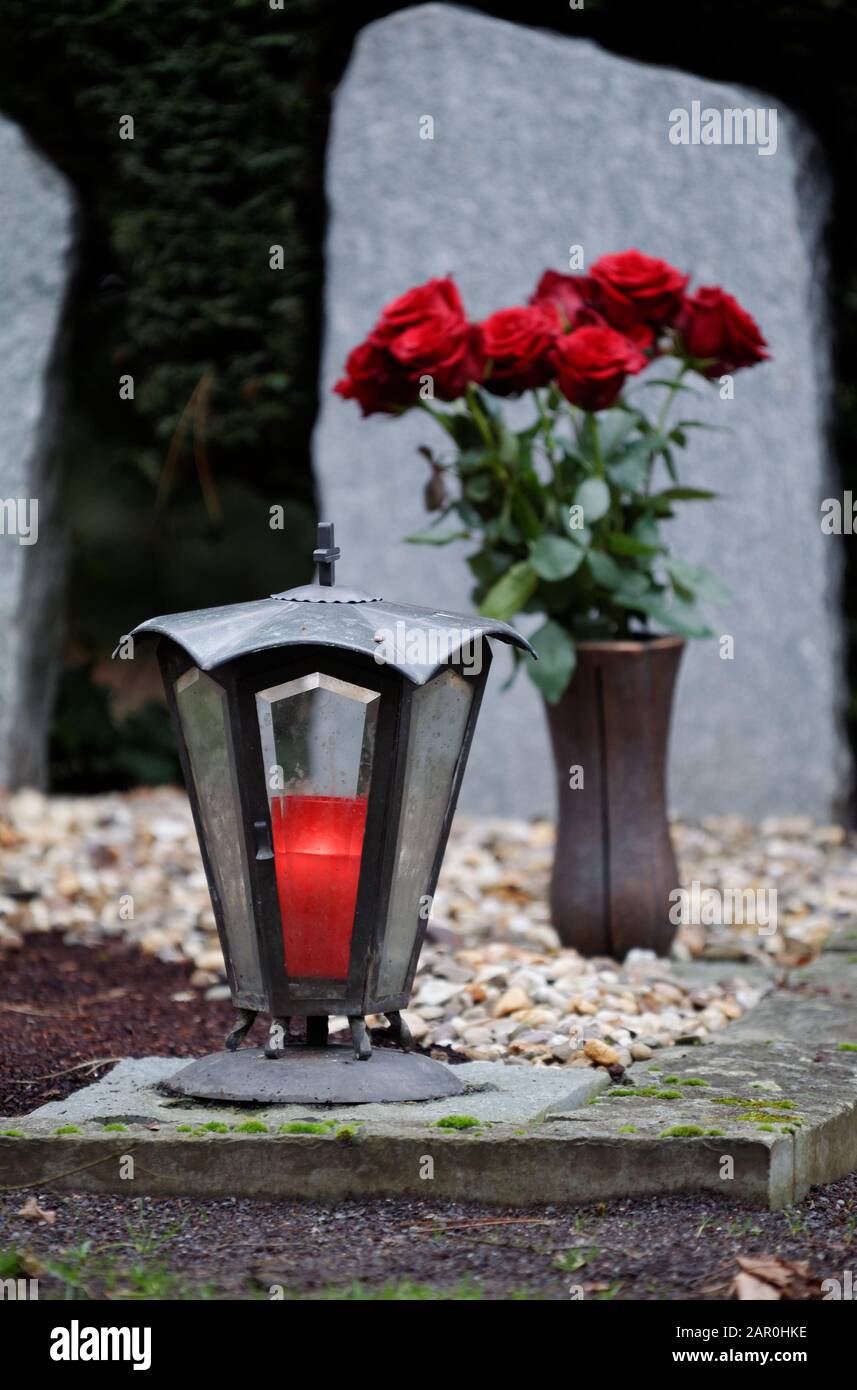 lanterna grave con candela bruciante su una tomba di fronte ad un bouquet di rose rosse in uno sfondo sfocato Foto Stock