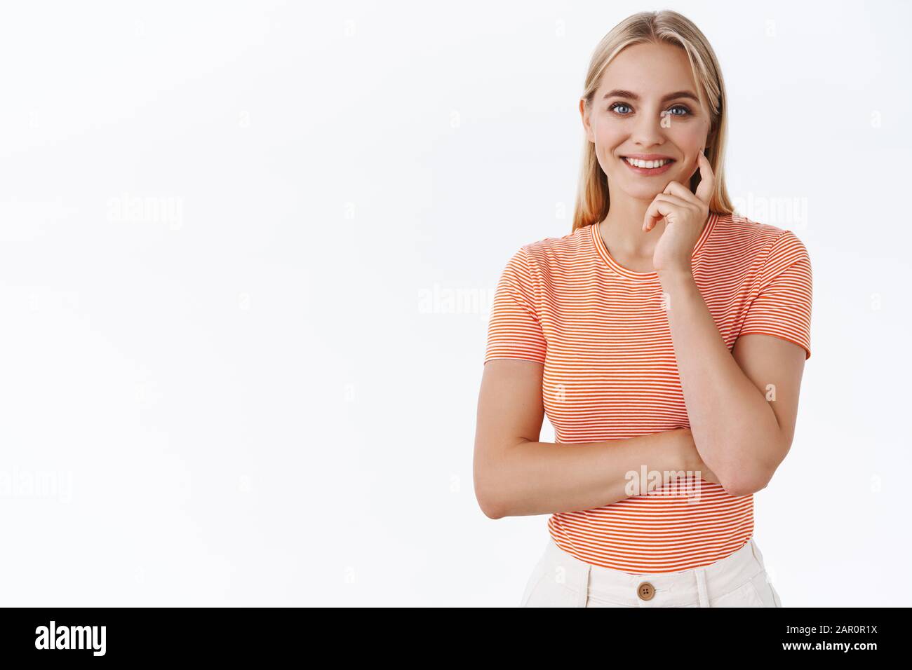 Donna femminile tenera dall'aspetto gradevole con capelli biondi, t-shirt a righe, croce una mano e tocco bella guancia guardare la macchina fotografica, guardare in modo affidabile e Foto Stock