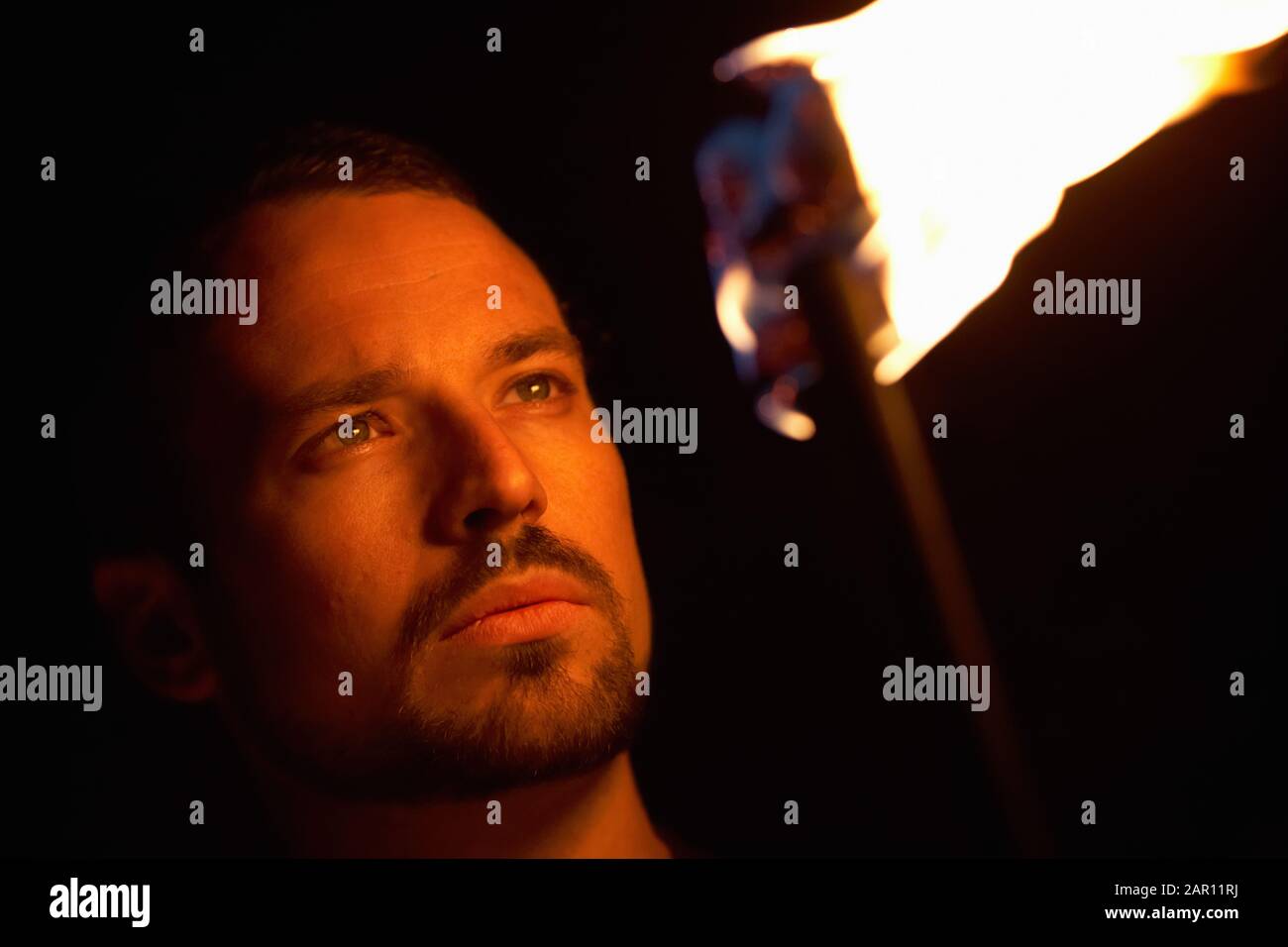 uomo che tiene fuoco torcia che fissa in fiamma con la faccia accesa dal fuoco Foto Stock