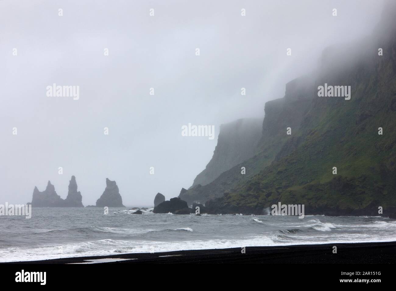 nebbia che rotola sopra la spiaggia di sabbia nera montagna reynisfjall e reynisdrangar rocce basaltiche stack di vik i myrdal sud islanda Foto Stock