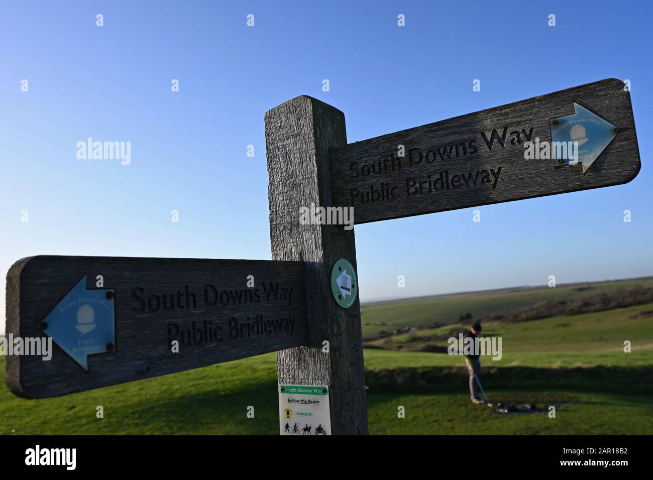 Segnaletica in legno che mostra la via di bridleway sul South Downs UK con un golfista, un campo da golf e le splendide colline del sud bassi sullo sfondo Foto Stock