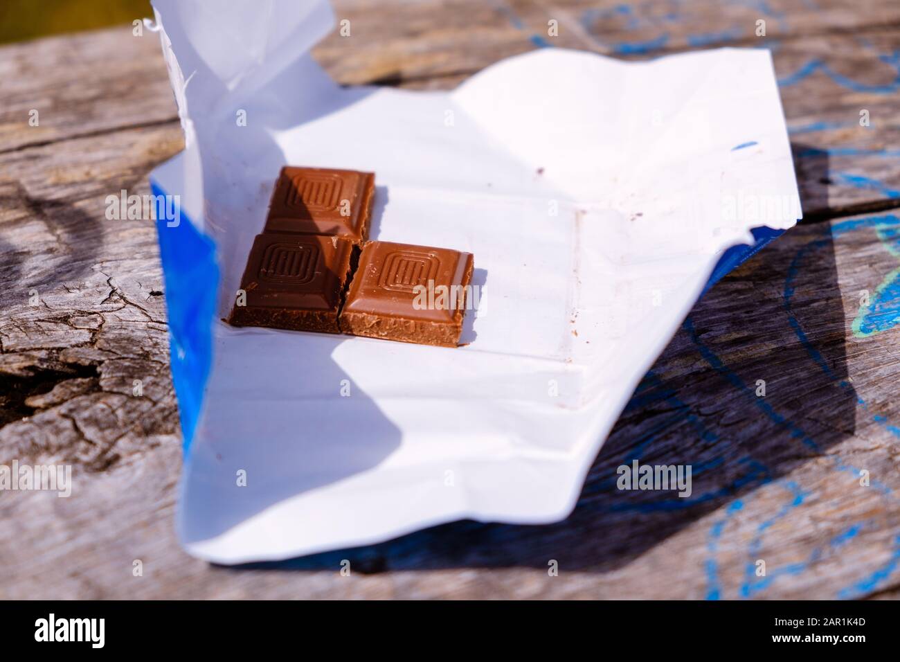 3 pezzi di cioccolato su carta imballaggio su un tavolo di legno all'aperto al sole. molto spazio di copia Foto Stock