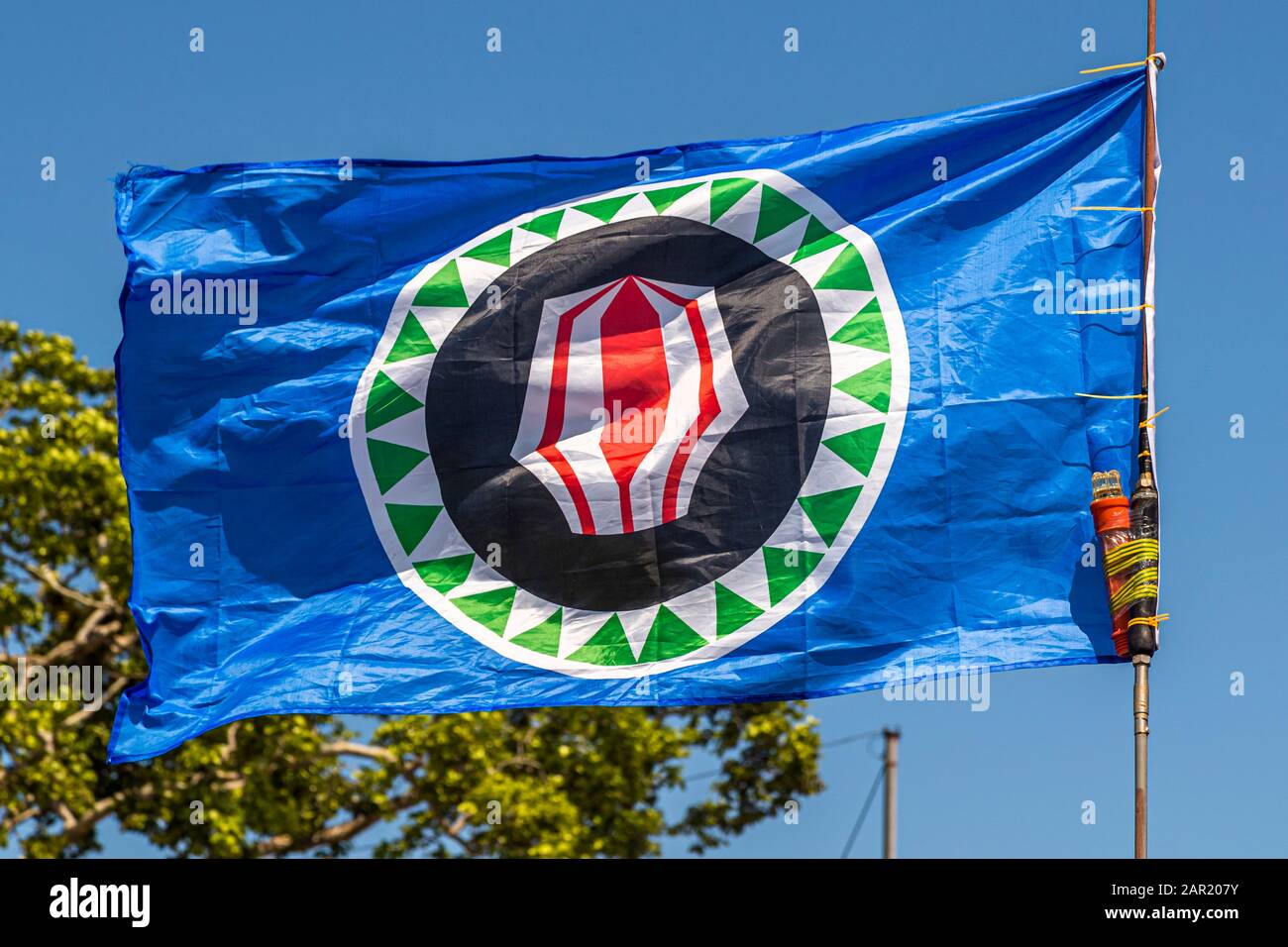 La bandiera della Regione Autonoma di Bougainville, Papua Nuova Guinea, riempie quasi l'intero fotogramma contro un cielo blu. L'emblema del corno di conchiglia rosso e bianco si staglia chiaramente. Foto Stock