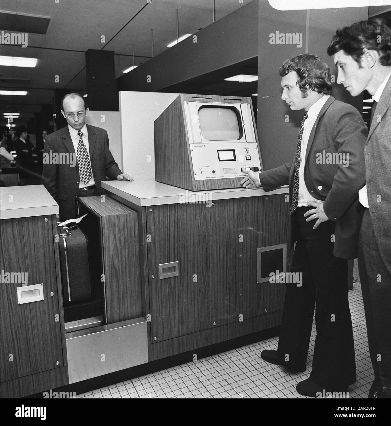 Dimostrazione di una macchina a raggi X a Schiphol per il controllo dei bagagli I Dipendenti guardano uno schermo mentre alcune valige passano il tunnel di controllo Data: 20 febbraio 1974 Località: North Holland, Schiphol Parole Chiave: Sicurezza, controlli, dimostrazioni Foto Stock