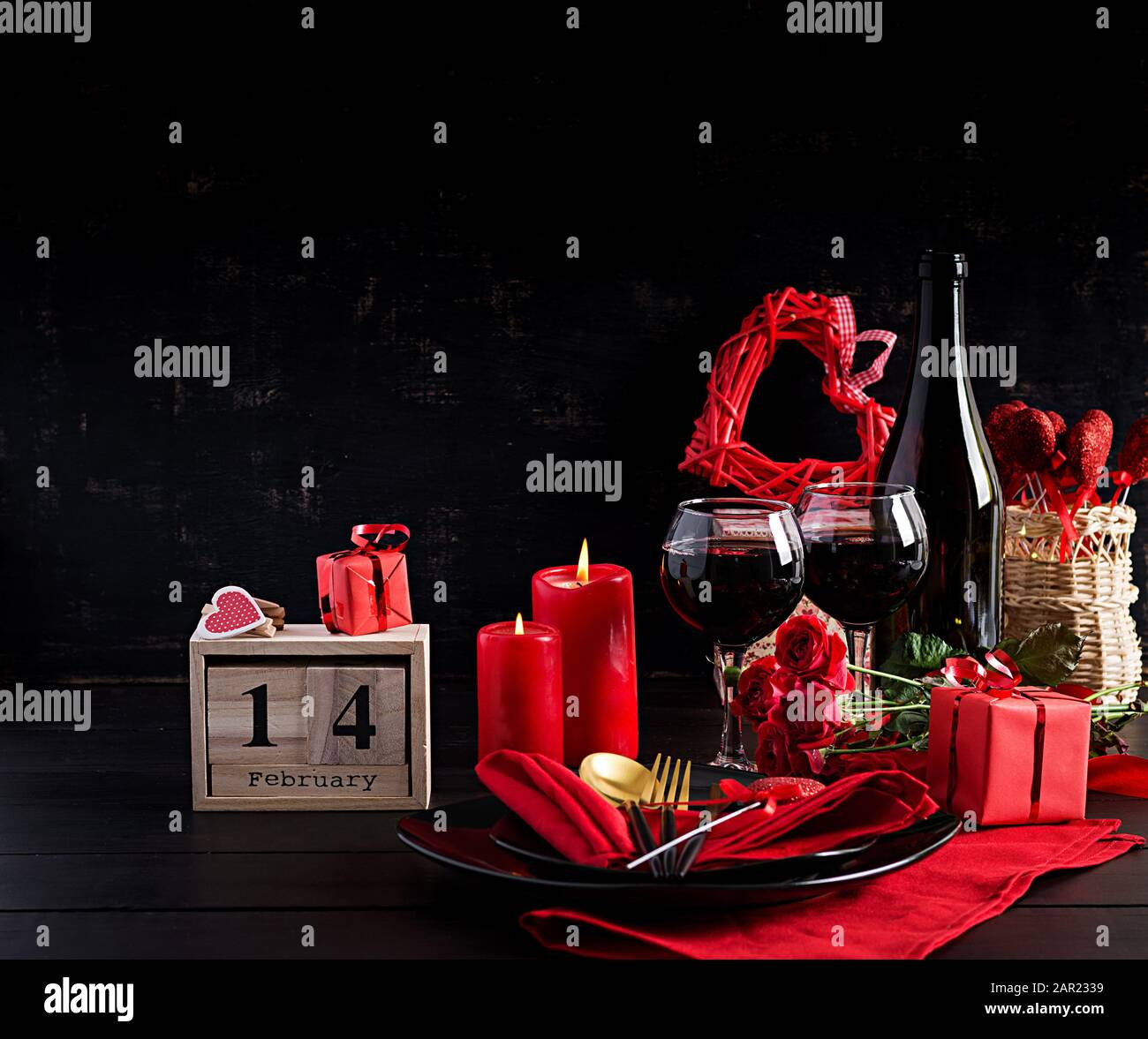 Cena di un giorno in San Valentino con tavolo con regalo, rose rosse, cuori con due wineglasses su sfondo scuro. Foto Stock