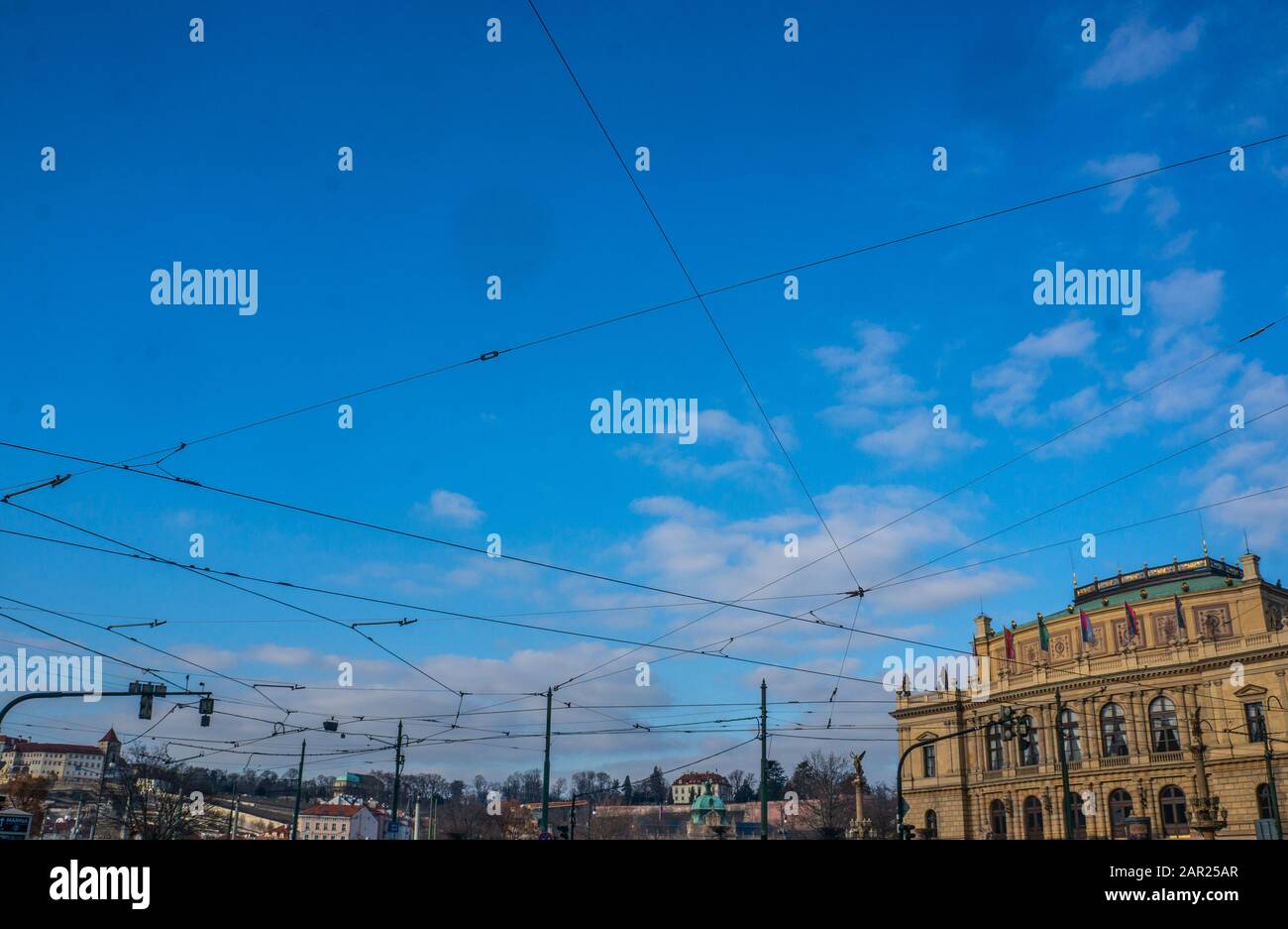 Cavi di alimentazione della linea del tram appesi sulla piazza alla Galerie Rudolfinum di Praga. Alimentazione elettrica aggrovigliata per i trasporti pubblici con cielo blu Foto Stock