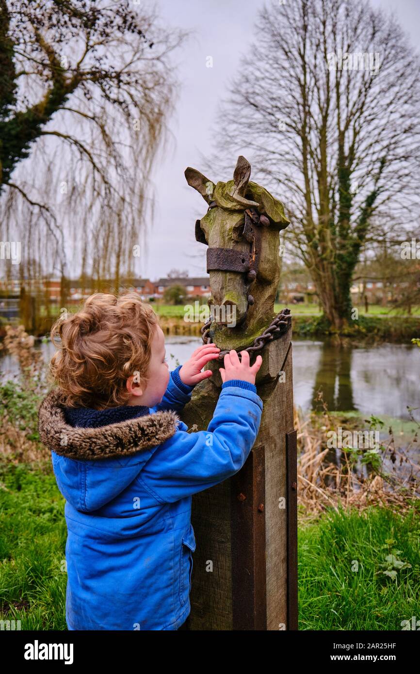 Un piccolo bambino che esamina una testa di cavalli di legno intagliato con Le sue mani sul lato del fiume Slea vicino Coglesford Mill Watermill Sleaford Lincolnshire Foto Stock