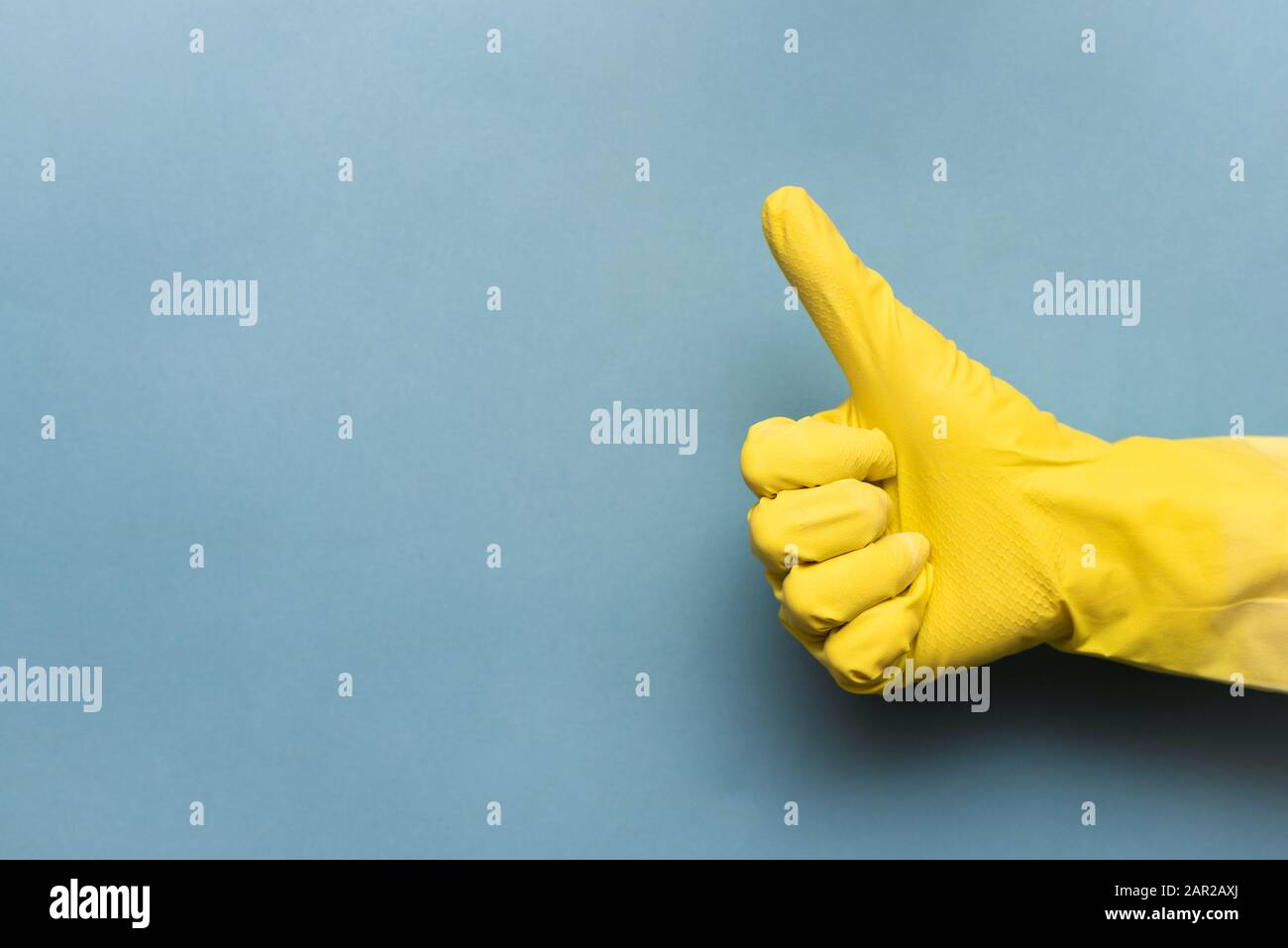 La mano femminile nel guanto di lavaggio mostra un gesto verso l'alto su sfondo blu. Foto Stock