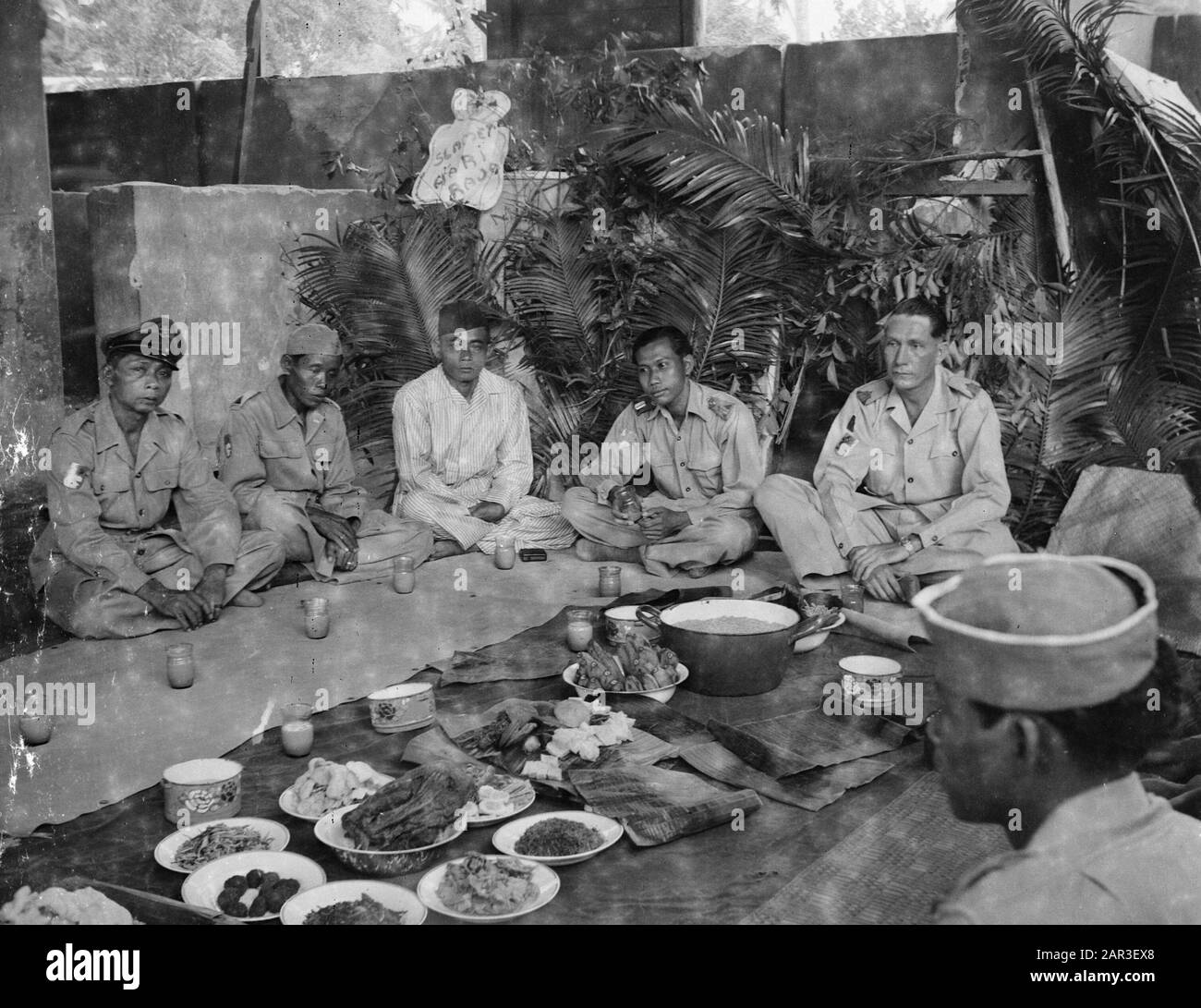 [Quattro soldati in lotuszit con una testa di villaggio? durante un selamatan? Annotazione: Tre di loro indossano l'emblema della U-Brigade. Il secondo uomo sulla destra quello del gabinetto del comandante dell'esercito? Il giudice ha posto i marchi KL gli altri tre della KNIL Data: 1947/01/01 luogo: Indonesia, Indie orientali olandesi Foto Stock