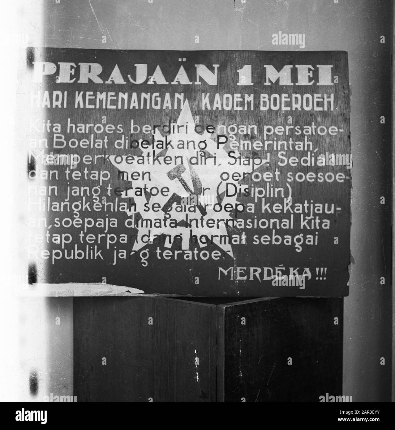 Foto di un poster con un'immagine di martello e falce e il testo: Perajo 1 maggio. Hari Kemenangan Kaoem Buruh / Kita haroer berdire delengan peratoean Bulat dibelakang Pemerintha. Mespercuckoo di. Siap! Siap! Ehi, Sedia! Poi tegtap menurut soesuhan jang teratoe [...] r (disiplin). Hilangkenlan segara roepa kekatjauan, supaja dimata internasional kita tetap terpa dang hormat sebagai Republik jang teratour. Merdeka!!! Date: 1947 Location: Indonesia, Dutch East Indies Foto Stock