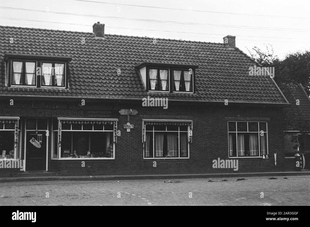 Servizio Culturale A Punti Fissi Hollum (Am). Negozio e casa alla Schoolstraat (Driesprong) (suddivisione Waterschap De Amelander Grieën) Annotazione: A-8. Segnaletica e segnale della fermata dell'autobus sul muro. Data: Ottobre 1953 luogo: Ameland, Friesland, Hollum Parole Chiave: Consolidamento del terreno, cambiamenti dell'acqua del terreno, negozi, case Foto Stock