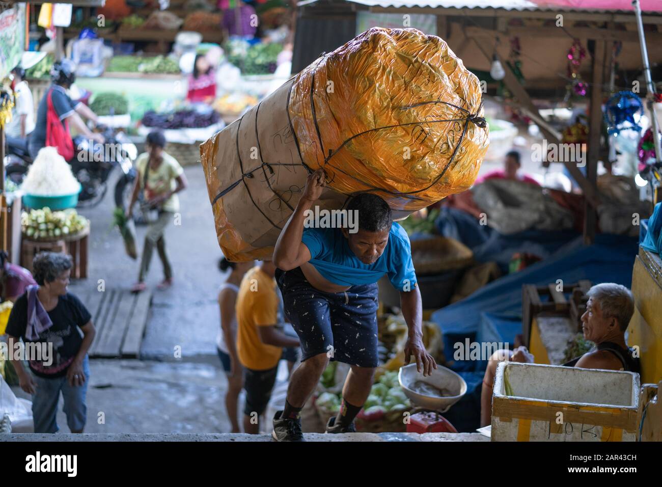 Un filippino uomo trasporta un carico pesante di ortaggi all'interno di un area di mercato di Cebu City, Filippine Foto Stock