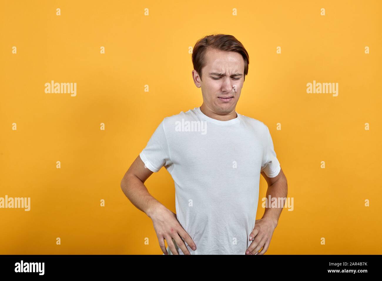 Giovane uomo con mal di schiena che tiene la schiena e il collo sullo sfondo giallo. Foto Stock