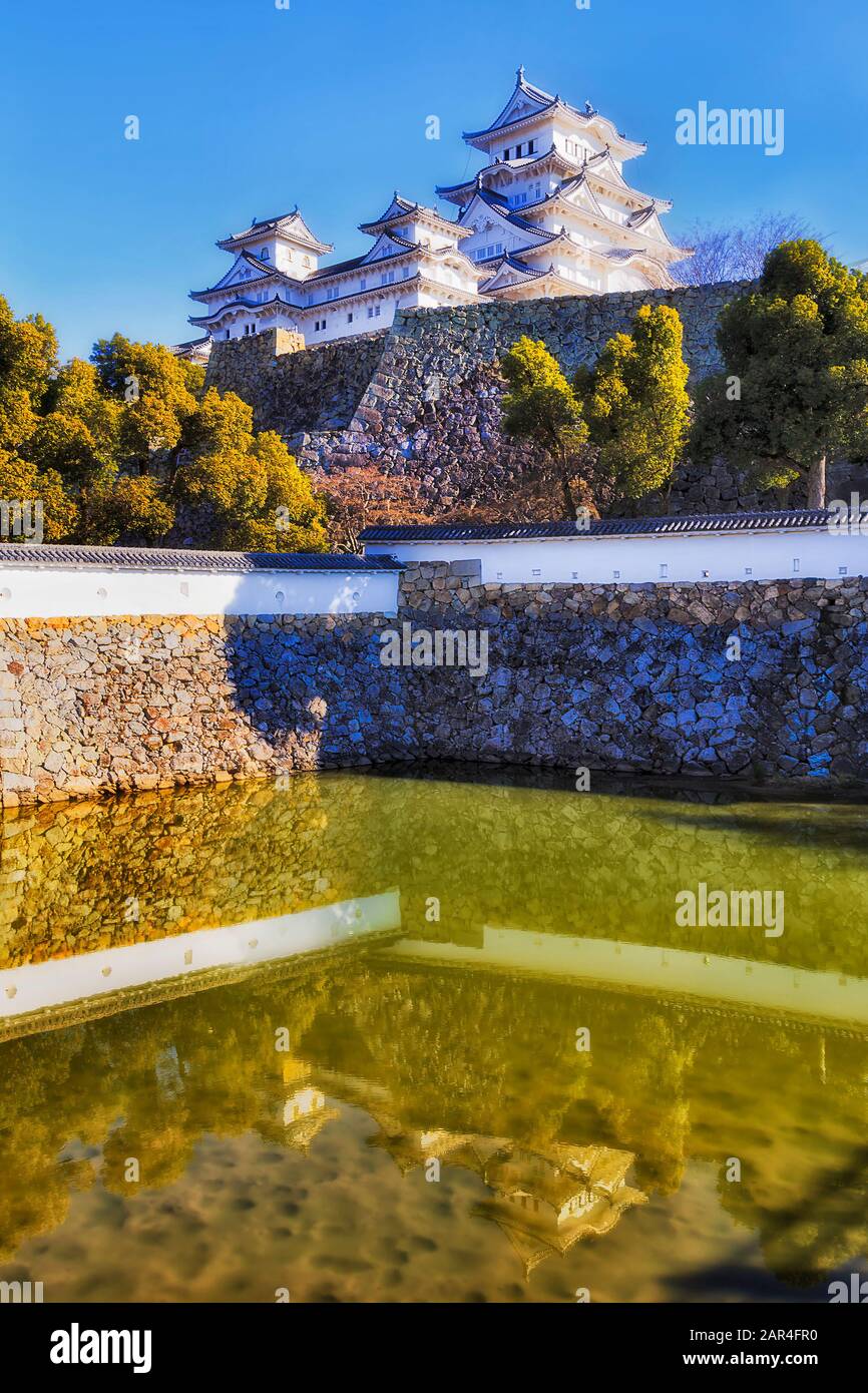 Himeji castello bianco in Giappone vicino Osaka in cima alle mura di pietra nel mezzo del grande parco - riflettendo in acque poco profonde del parco stagno. Foto Stock