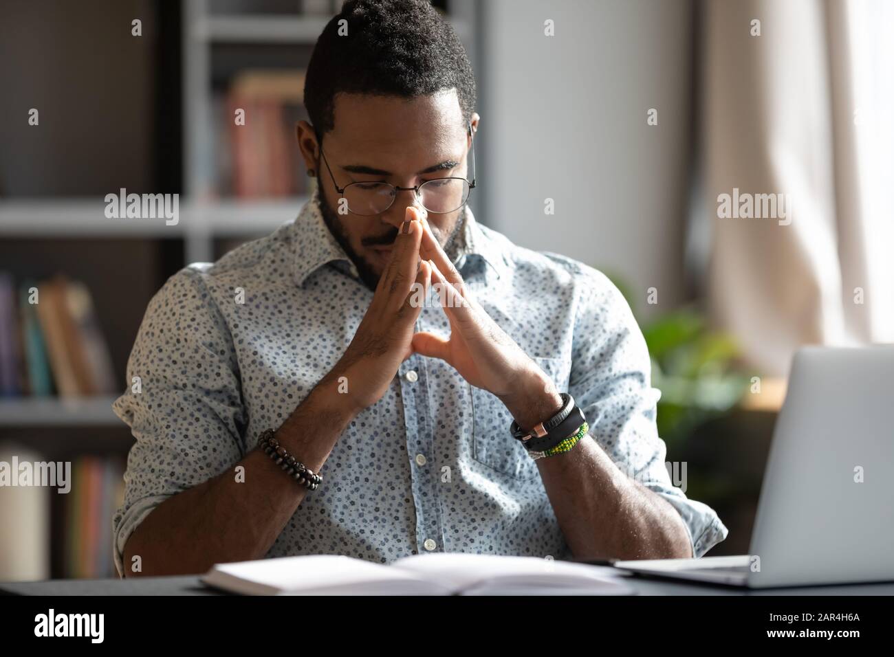 Giovane uomo d'affari americano africano che prega sedersi al banco di lavoro Foto Stock