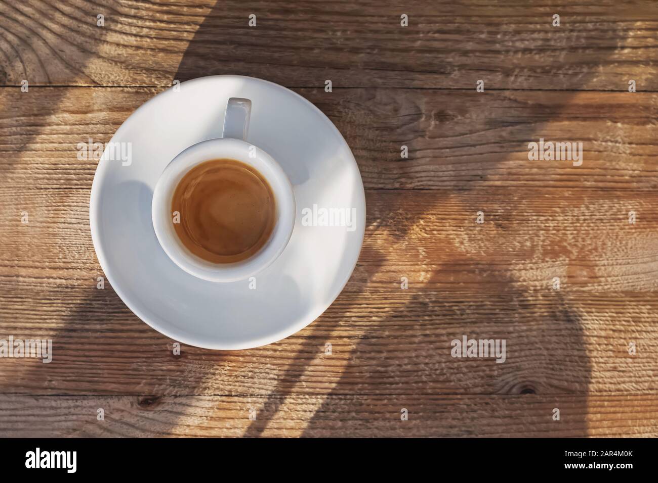 Tazza di caffè in piedi sul tavolo in legno e alla luce del sole con ombre che cadono Foto Stock