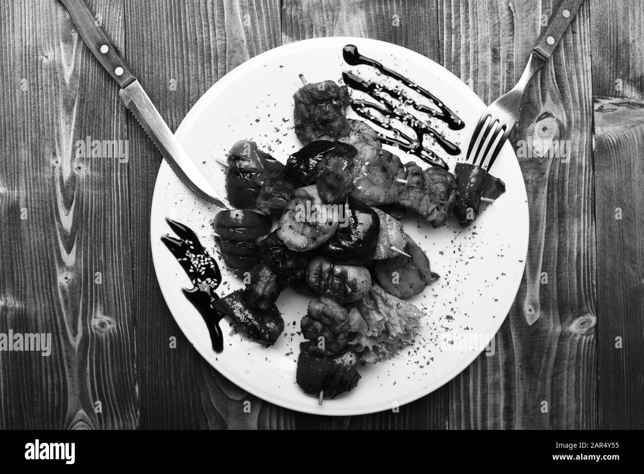 Tavolo servito per uno in ristorante o caffetteria. Arrosto di maiale e verdure alla griglia su sfondo di legno. Cucina tradizionale. Forchetta e coltello vicino a un piatto sofisticato con salsa di soia. Foto Stock