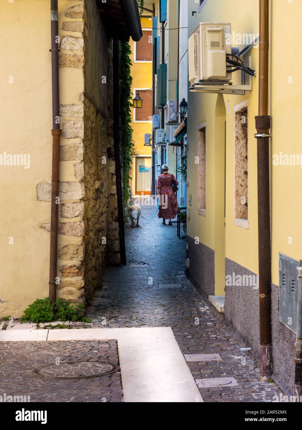 Una donna che cammina un cane su una strada molto stretta tra edifici gialli Foto Stock