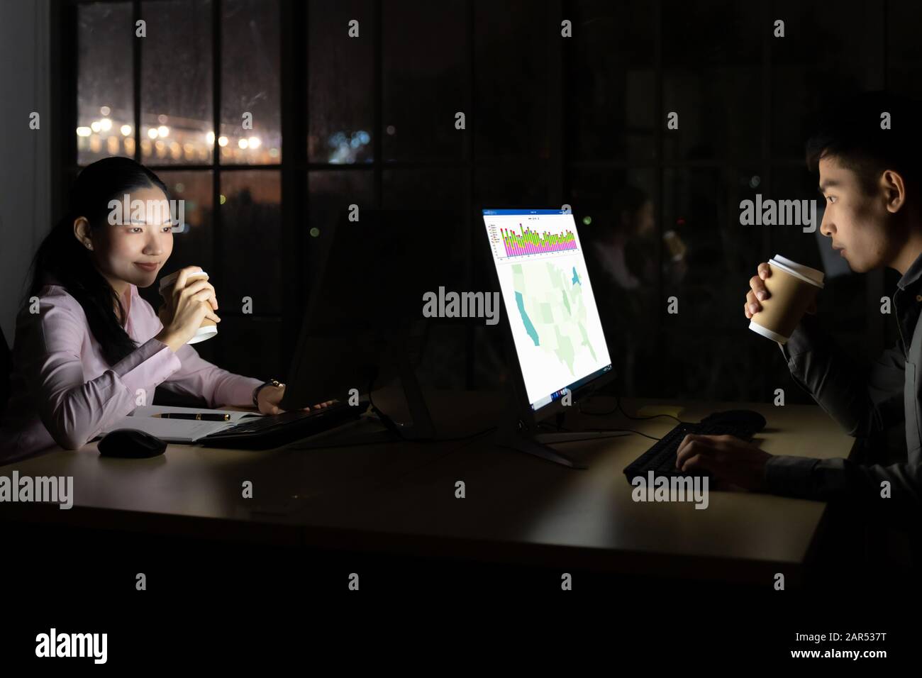 Giovane adulto uomo d'affari asiatici e la donna a bere il caffè caldo mentre si lavora a tarda notte nel loro ufficio con computer desktop e laptop. Utilizzo come disco Foto Stock