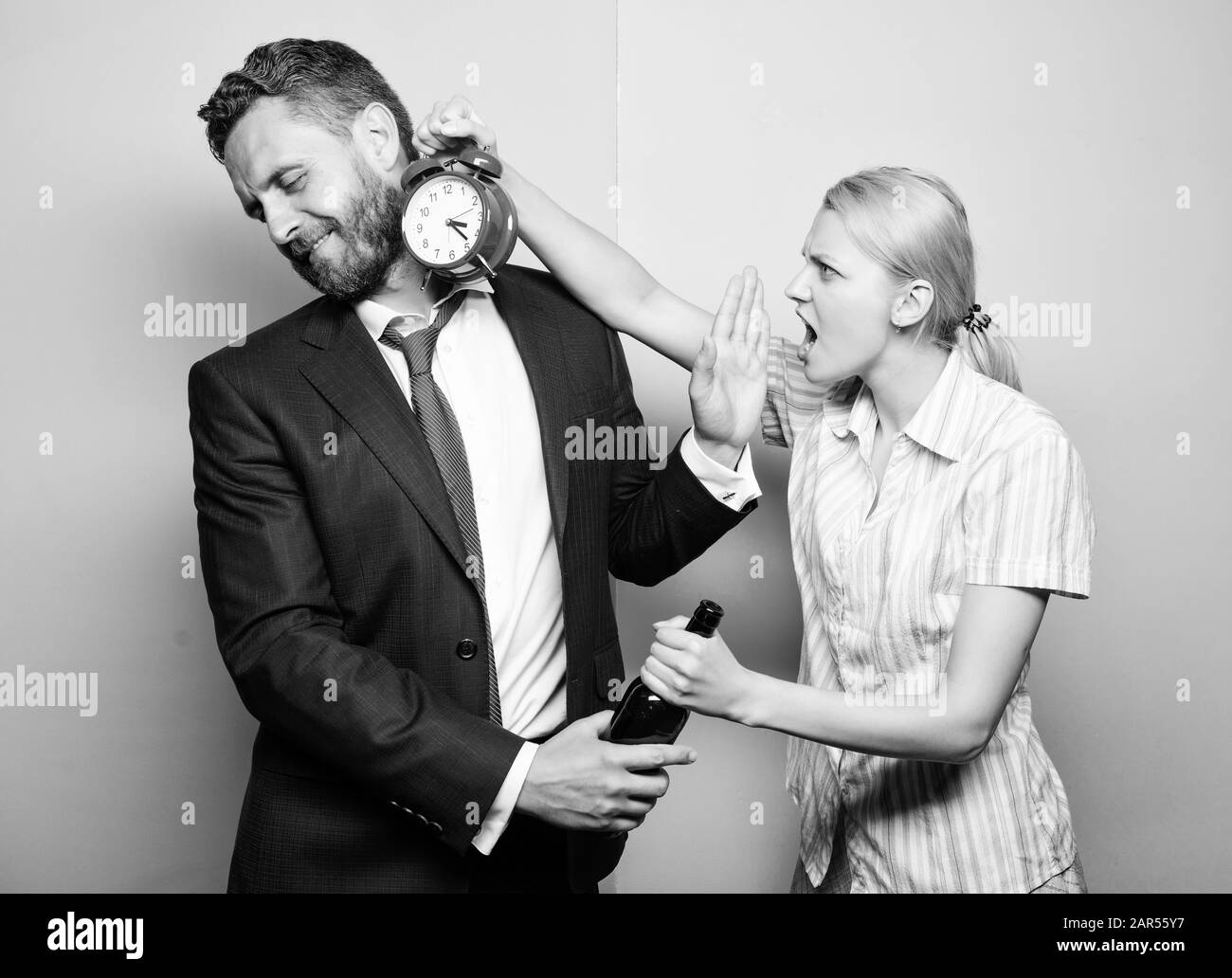 A che ora è. Imprenditore con bottiglia di alcool e la donna con la sveglia. L uomo che soffre di alcolismo. Arrabbiato moglie incontro ubriaco marito tardi a casa. Dipendenza alcolismo o abuso di alcool. Foto Stock