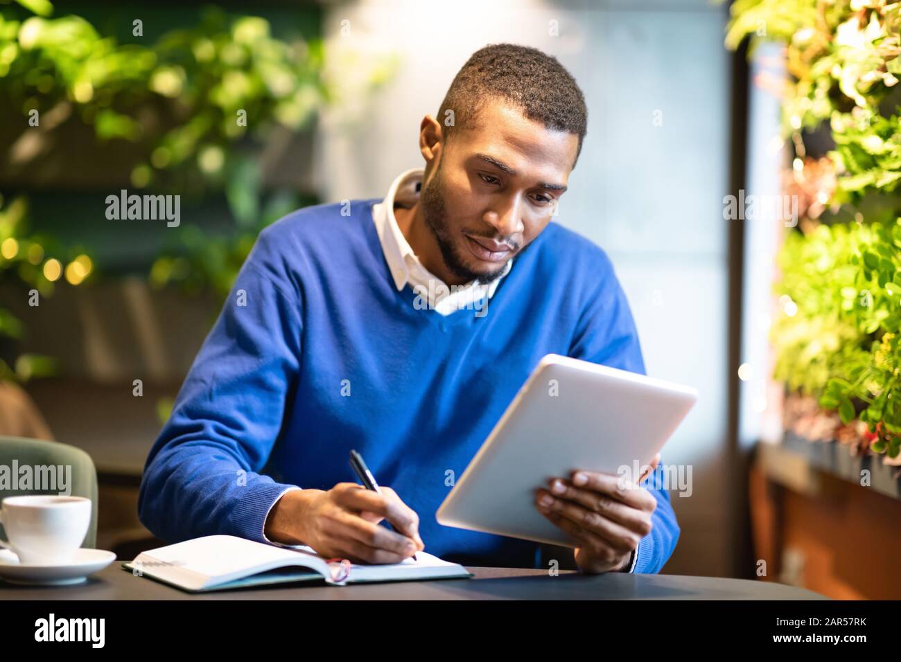 Uomo nero che tiene il tablet e scrive nel notebook Foto Stock