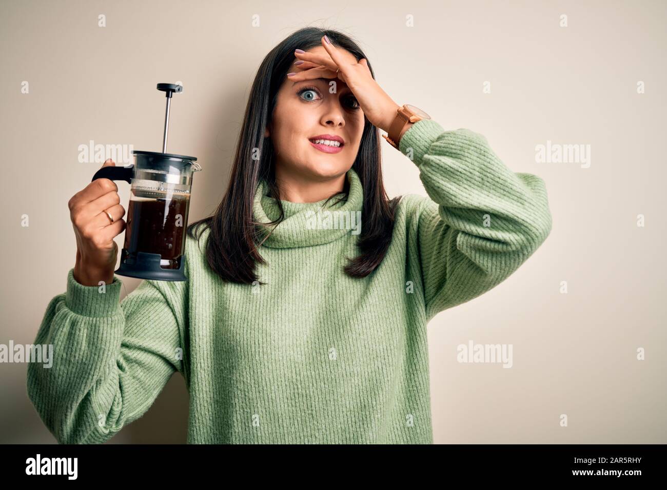 Giovane donna con occhi blu che fa caffè utilizzando il creatore di caffè in piedi su sfondo bianco stressato con la mano sulla testa, scioccato con vergogna e sorpresa fa Foto Stock