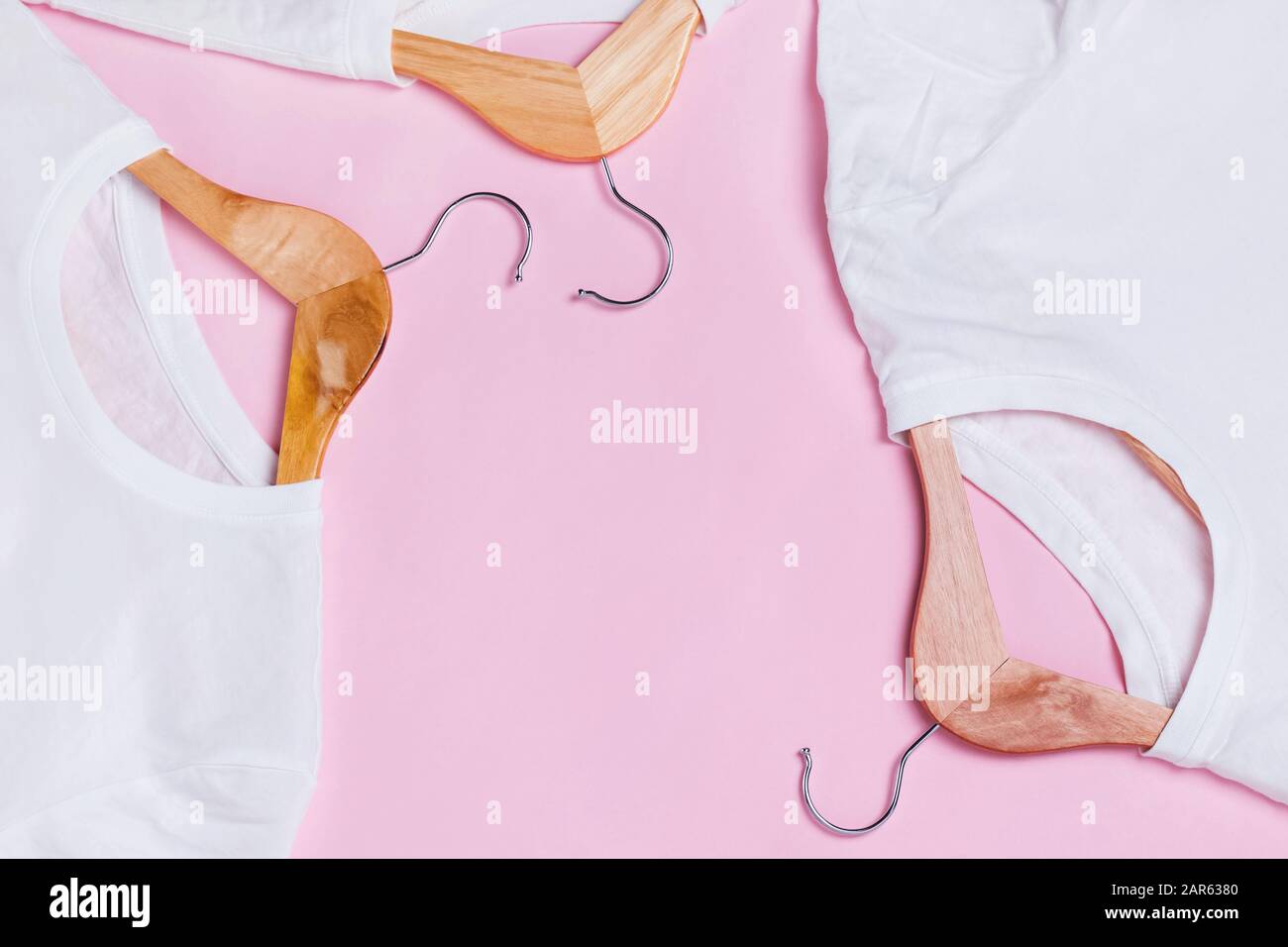 T-shirt bianche su appendiabiti in legno su sfondo rosa Foto Stock