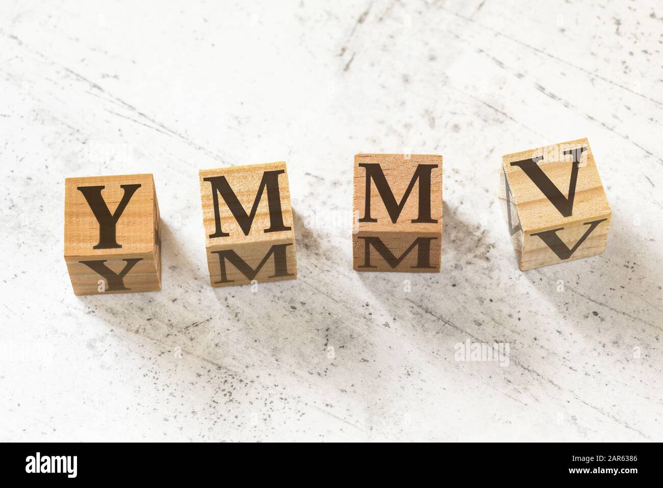Quattro cubetti di legno con lettere YMMV, il che significa che il chilometraggio può Variare sulla lavagna bianca. Foto Stock
