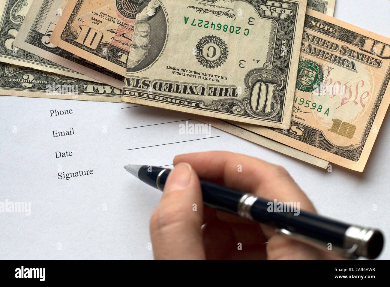 Una persona che firma un documento, un contratto, un contratto. Sfondo dollaro. Una pagina con testo: Telefono, e-mail, Data, Firma Foto Stock