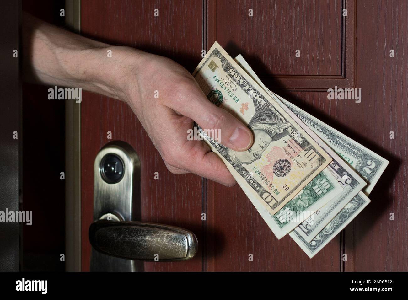 Una mano maschio dà una tangente da dietro una porta socchiusa. Concetto di corruzione, criminalità, frodi finanziarie Foto Stock