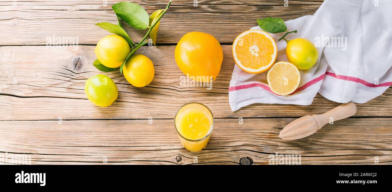 Limoni freschi e arance con foglie verdi su sfondo di legno, succo di agrumi e spremiagrumi, striscione lungo Foto Stock