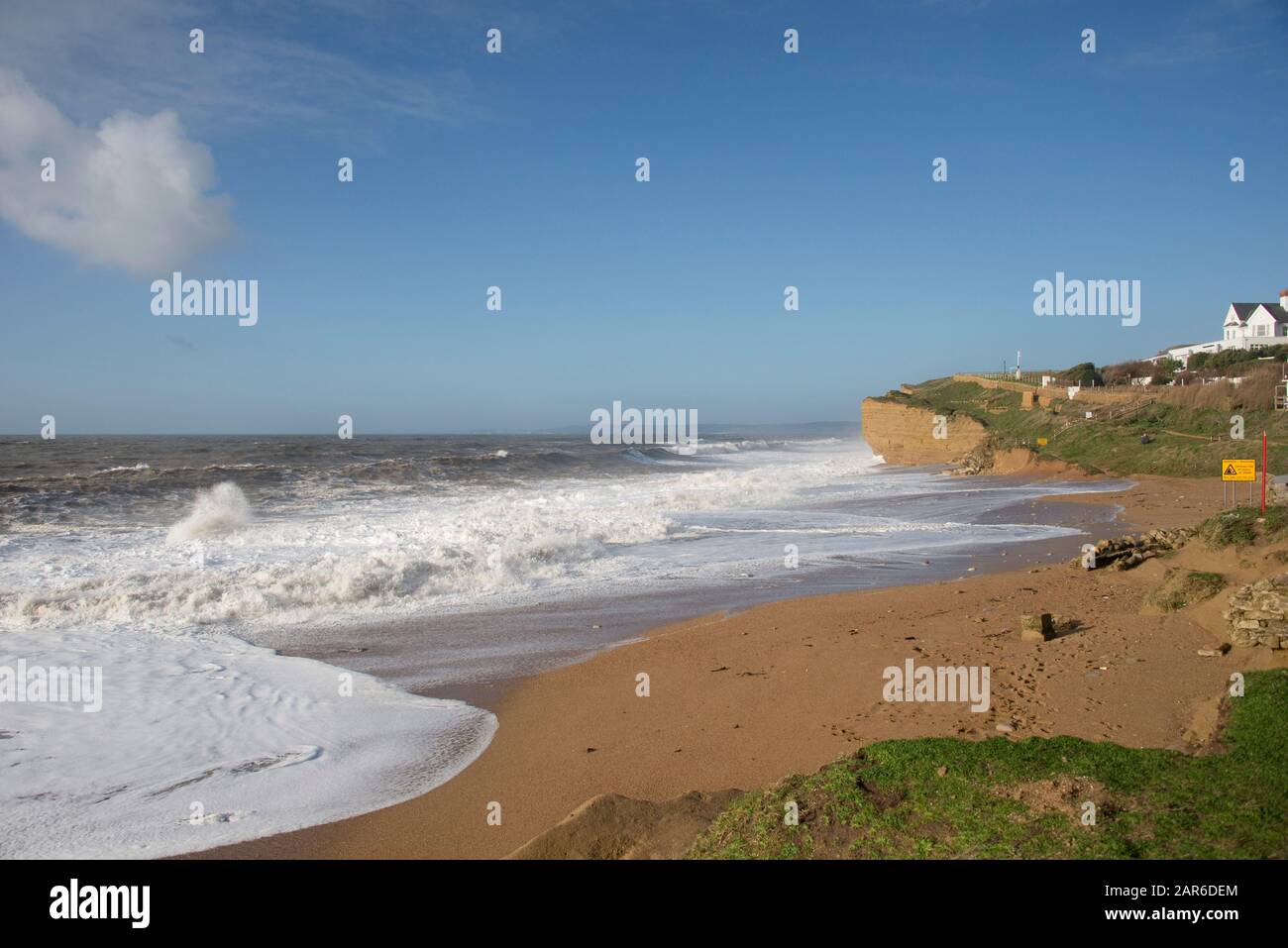Alte onde bianche che si infrangono sulla spiaggia e sulle scogliere di arenaria durante l'alta marea in una bella giornata a Hive Beach, vicino West Bay, Dorset, gennaio Foto Stock