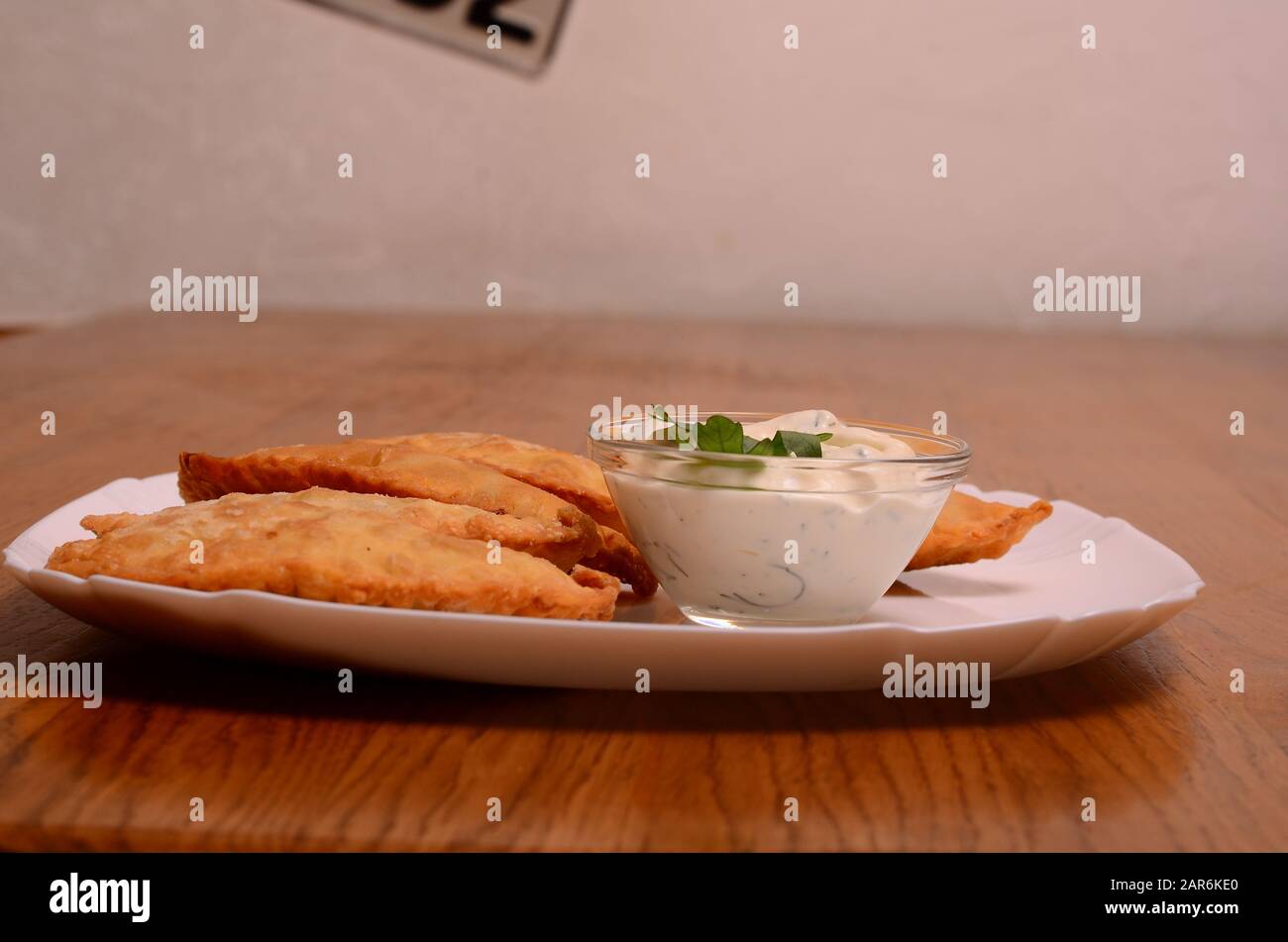 Cucina uzbeka orientale Tatar, cheburek con carne e suluguni formaggio in un piatto bianco con verdure e verdure su un tavolo di legno. Foto Stock