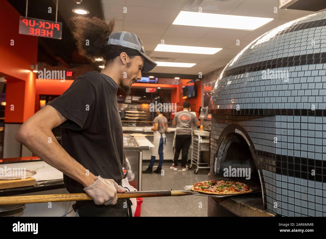Detroit, Michigan - un operaio fa cuocere una pizza in un forno di mattoni al Flamz Pizzeria nel quartiere Morningside della città. Il ristorante offre un ristorante Foto Stock