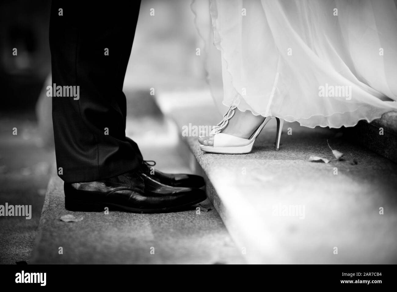 la sposa e lo sposo si levano in piedi l'uno di fronte all'altro sui gradini, nella cornice soltanto le gambe, intorno sono cadute le foglie di autunno. nero e bianco. primo piano Foto Stock